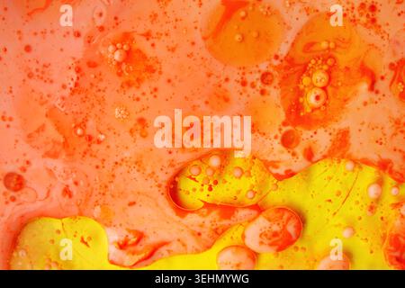 Abstract macro of oil and water bubbles forming floating spheres on a vibrant orange and yellow background, with soft gradients, and organic texture. Stock Photo