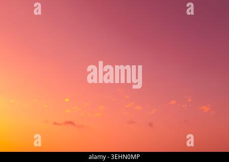 Soft pastel sunset sky with warm orange, pink, and purple gradient and thin scattered cloud near the horizon, creating a calm minimal background with Stock Photo