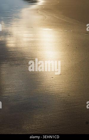 A serene beach scene with smooth golden sand reflecting the soft ambient light. The gentle waves create delicate patterns on the shore, emphasizing tr Stock Photo