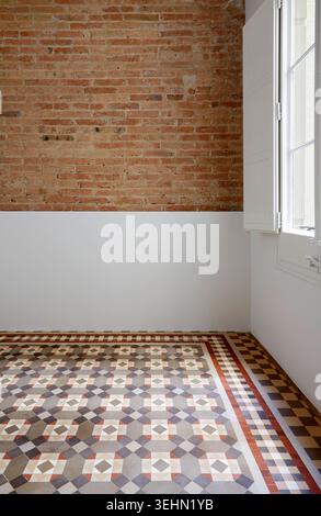 Bright empty interior with exposed brick accent wall, white window frame, and geometric mosaic tile floor, offering a clean backdrop for home staging Stock Photo