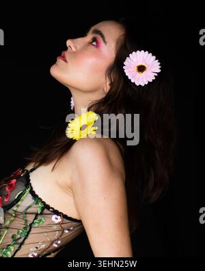 A creative portrait features a woman against a dark background with delicate pink and yellow flowers in her hair, highlighting her expressive profile Stock Photo