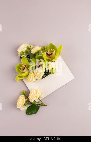 Minimal floral envelope mockup on a beige background, filled with cream roses and green orchid blooms. Elegant flat lay composition for wedding invita Stock Photo
