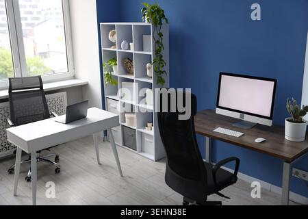Desks with computers, chairs, shelving unit and decor in office. Interior design Stock Photo