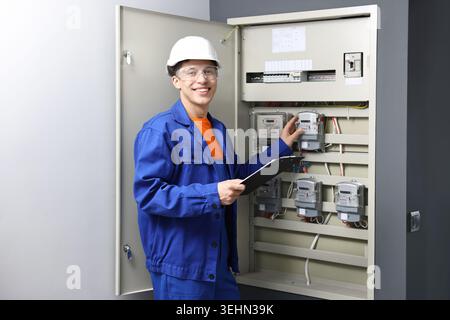 Electrician with clipboard checking electrical meters in fuse box indoors Stock Photo