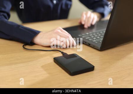 Woman connecting external hard drive to laptop at wooden desk, closeup Stock Photo