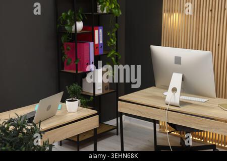 Wooden desks with computers, stationery, plants and shelving unit in office. Interior design Stock Photo