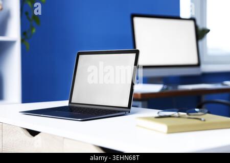 Desks with computers, glasses and stationery in office, closeup Stock Photo
