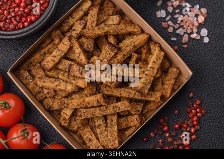 Food, Crispy homemade brown bread crackers or croutons with seeds and grains, salt, spices and herbs on a dark concrete background Stock Photo