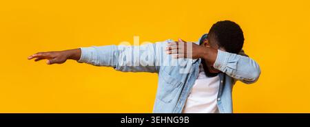 Man throwing dab, making internet meme pose on yellow background Stock Photo