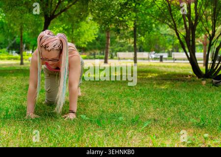 Yoga instructor demonstrating cat-cow pose on mat outdoors in green summer park for students. Cat-cow pose, yoga, instructor, mat, summer, outdoors. Stock Photo