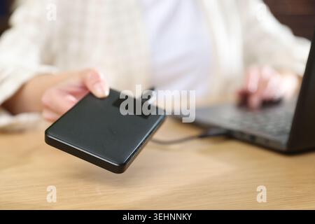 Woman connecting external hard drive to laptop at wooden desk, closeup Stock Photo