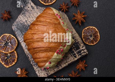 Food, Crispy sweet red croissant with pistachio, raspberry and strawberry on a dark concrete background Stock Photo