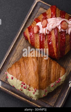 Food, Crispy sweet red croissant with pistachio, raspberry and strawberry on a dark concrete background Stock Photo