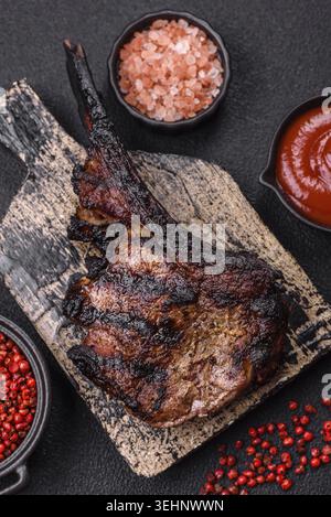 Food, Juicy grilled beef tomahawk steak with salt, spices and herbs on a dark concrete background Stock Photo