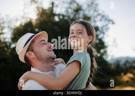 Happy father holding smiling daughter outdoors during family time. Stock Photo