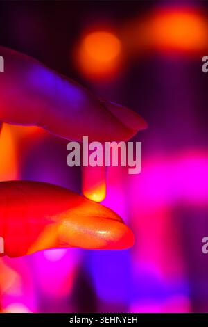 Close-up view of a hand grasping a white capsule, with a colorful blurred background featuring vibrant purple and orange lights. Neon Pharma Aesthetic Stock Photo
