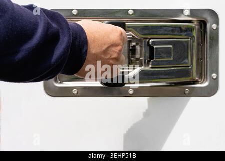Close up of a person opening a silver metal latched compartment door on a vehicle Stock Photo