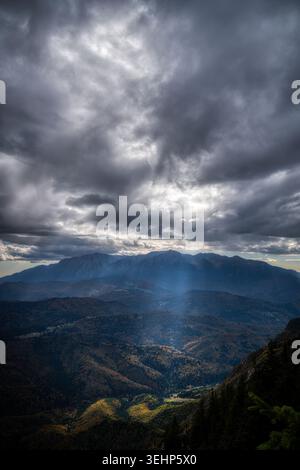 Sunbeams breaking through dark storm clouds over autumn mountain peaks near Brasov, Romania Stock Photo