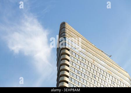 Low angle view of modern triangular corporate building corner against blue sky with light clouds. Futuristic glass skyscraper facade with copy space f Stock Photo