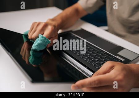Close-up hands of unrecognizable person cleaning laptop screen and keyboard with microfiber cloth, maintaining hygiene for remote work and technology Stock Photo