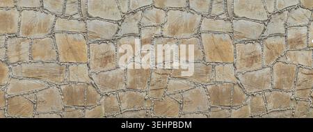 Rough textured brown and gray stone masonry wall with irregular shapes and cement joints Stock Photo