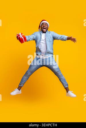 Overjoyed afro guy in santa hat jumping with gift box Stock Photo