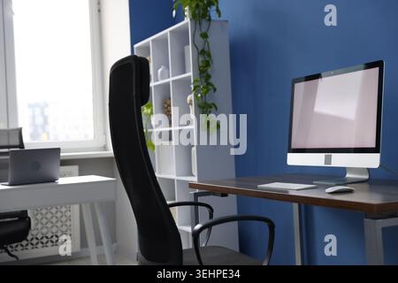 Desks with computers, chair, shelving unit and decor in office. Interior design Stock Photo