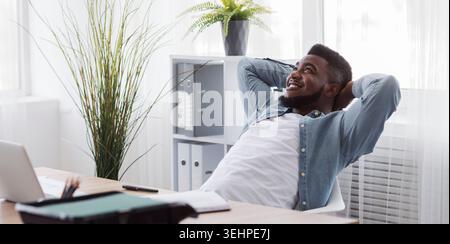 Black employee resting from office work, leaning back on chair Stock Photo