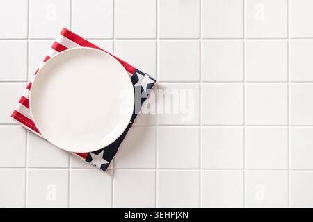 Minimal Patriotic table setting with empty white plate and American themed napkin on white tile background with copy space. Stock Photo