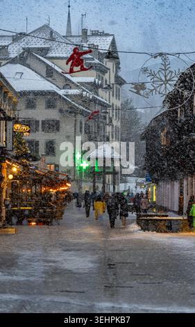 People walking through a snowy street during heavy snowfall in a European alpine town decorated for winter holidays. Stock Photo