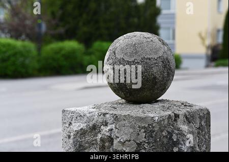 A minimalist close-up photograph of a weathered stone sphere resting on a concrete pedestal, highlighting rough textures, geometric form, and urban ar Stock Photo