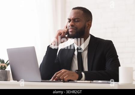 Pensive black businessman working with laptop in office Stock Photo