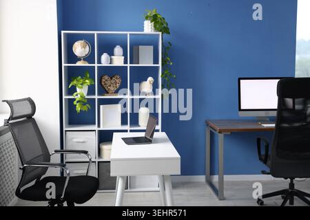 Desks with computers, chairs, shelving unit and decor in office. Interior design Stock Photo
