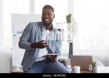 Smiling black manager holding digital tablet, explaining something to his colleagues Stock Photo