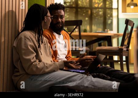 Happy black people having fun on the weekend indoors sitting on the floor together and using a laptop. Man and woman share love, bonding and togetherness, peaceful authentic domestic life. Stock Photo