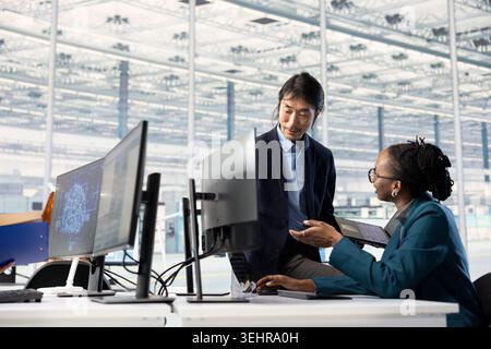 Asian man and african american woman in microchip factory RD office training AI model to optimize hardware. Diverse coworkers use artificial intelligence to improve manufacturing efficiency Stock Photo