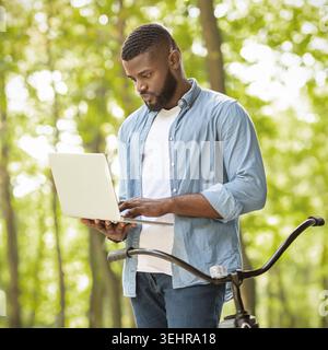 Rush Job. Focused afro businessman standing outdoors and using laptop Stock Photo