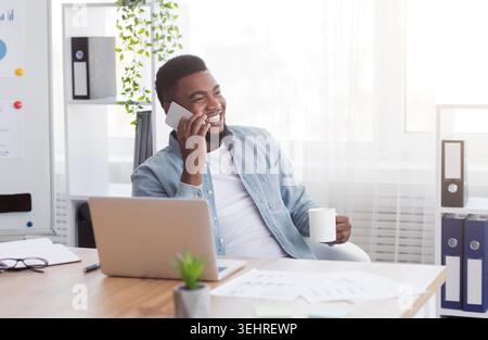 Handsome businessman talking on phone and drinking coffee in office Stock Photo