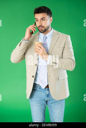 Adult man talking on phone and drinking coffee in front of green screen Stock Photo