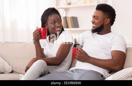 Joyful Afro Couple Relaxing With Coffee Sitting On Couch At Home Stock Photo