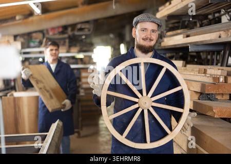 Portrait of an experienced carpenter holding wooden cart wheel in his hands Stock Photo