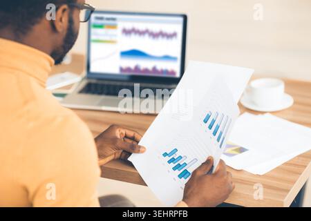 Black manager working with diagrams on pc and paper Stock Photo