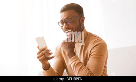 Cheerful man using phone chatting online sitting on sofa, panorama Stock Photo