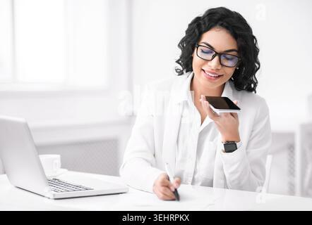 Smiling hispanic woman using voice assistant on phone Stock Photo