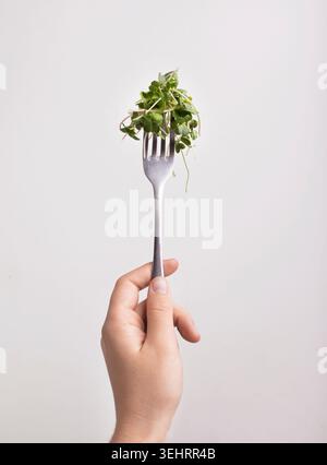 Micro green on fork in female hand over white background Stock Photo