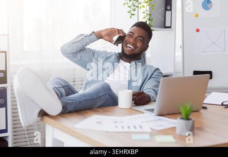 Joyful black manager talking on phone while having break at work Stock Photo