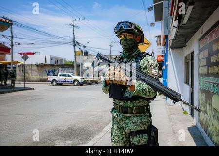 A mexican military in camouflage uniform and covered face holds an assault rifle while guarding a cordoned-off city street. Stock Photo