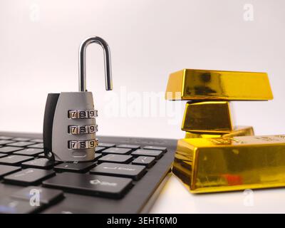 A silver combination padlock unlocked on a keyboard next to a stack of shiny gold bars. Stock Photo