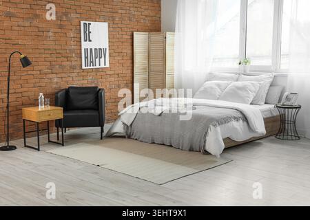 Interior of hotel room with armchair, clean towels and bathrobe on bed Stock Photo