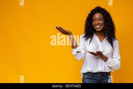 Smiling Woman in White Shirt Presenting Against Vibrant Yellow Background Stock Photo